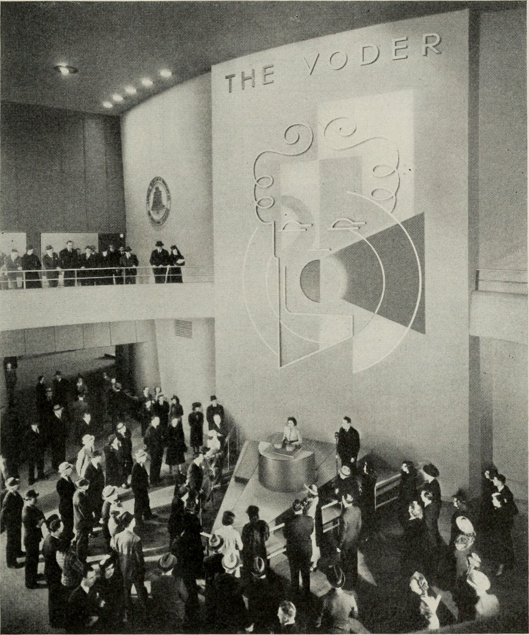 1939年ニューヨーク万国博覧会のベル研究所ブースでVODERが実演される様子。壁面に大きく THE VODER と掲げられ、オペレーターが鍵盤の前に座り、大勢の見物客が取り囲んでいる